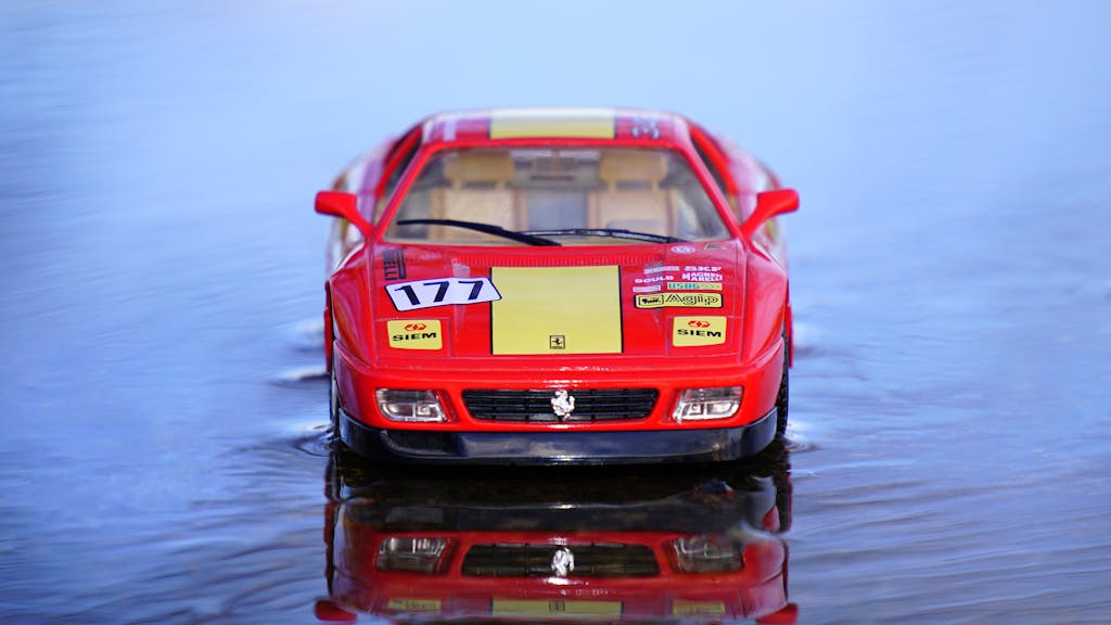 A striking red Ferrari model toy car captured on a reflective water surface, showcasing its design.