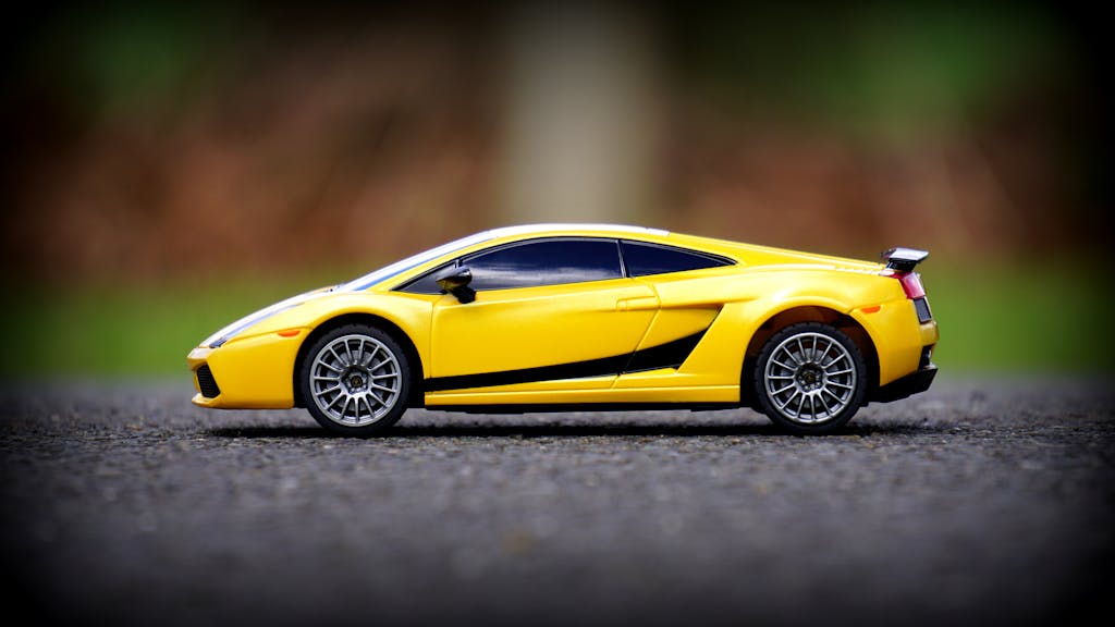 Close-up of a yellow toy car resembling a sports car model on asphalt with blurred background.